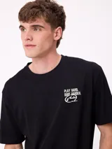 Remera de corte holgado color crema con estampado gráfico en la espalda que incluye el número 85, personajes animados y la frase Play Hard, Surf Harder.