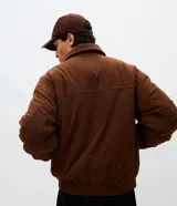 Campera bomber de pana color marrón, con cuello polo, cierre frontal con cremallera y puños y bajo elásticos.