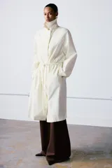 Trench oversize de cuello solapa y manga larga, con cintura ajustable mediante cordones y cierre frontal oculto. Cuenta con bolsillos laterales y forro interior.