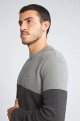 Sweater de punto con diseño color block en tonos gris claro y gris oscuro, de cuello redondo y manga larga. Presenta un pequeño logo bordado en el pecho.
