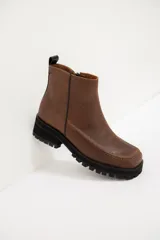 Botas cortas de cuero color visón, con suela track negra y costuras decorativas en contraste a lo largo del empeine. Cuentan con cierre lateral para facilitar su colocación.