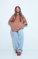 Remera de corte oversize color marrón con efecto gastado, manga corta y estampa gráfica retro en el frente.