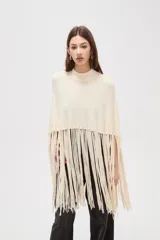 Poncho de punto color crudo con cuello alto y diseño de flecos largos en el ruedo.
