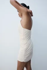Vestido mini palabra de honor color crudo, con diseño drapeado en diagonal y cierre lateral con cremallera oculta.