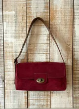 Cartera de hombro color bordó con textura tipo cocodrilo, confeccionada en cuero. Presenta un diseño rectangular con solapa frontal, cierre metálico giratorio en tono bronce y correa de hombro ajustable en cuero color marrón.