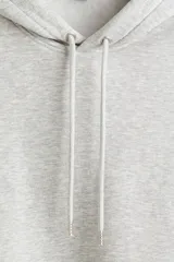Canguro gris con capucha forrada con cordón ajustable, hombros caídos, bolsillo tipo canguro y corte holgado.