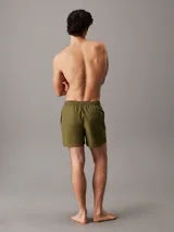 Short de baño verde militar con cintura elástica ajustable con cordón y logo de Calvin Klein estampado en blanco en la pierna izquierda.