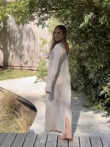 Vestido largo color crudo, de tejido de algodón fino y ligero, con escote en V y mangas largas acampanadas. Se puede usar con el escote hacia adelante o hacia atrás.