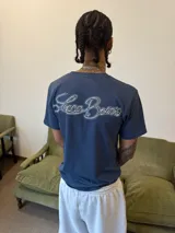 Remera de algodón color azul con estampa gráfica blanca en el pecho y etiqueta pequeña en la manga.