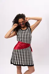 Vestido tejido de punto con rayas verticales en blanco y negro, sin mangas y con abertura en la espalda. Incluye un pañuelo rojo con lunares negros atado a la cintura.