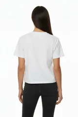 Remera blanca de algodón con cuello redondo y manga corta. Estampado frontal con la palabra "MERCI" en negro con efecto de puntos o tachas.