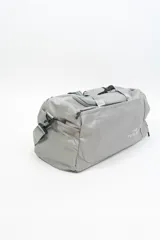 Bolso de viaje gris con doble asa corta y cierre superior. Estampado frontal con la frase "The Tote Bag" en letras blancas.