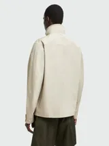 Chaqueta acolchada color beige con cuello alto, cierre con botones a presión, cuatro bolsillos frontales con solapa y puños abotonados.