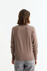 Sweater de punto liso color marrón topo, con cuello redondo y manga larga. Presenta un detalle de tres botones pequeños en la abertura del puño.
