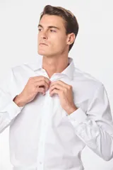 Camisa blanca lisa de vestir con cuello clásico, manga larga y corte slim fit. Confeccionada con 60% algodón, 37% poliéster y 3% spandex. Cuenta con pinzas en la espalda en talles XL al XXX, botones personalizados y logo bordado en el pecho.