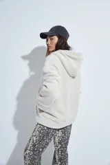 Canguro de corderito con capucha, cierre frontal y bolsillos laterales. Diseño relajado y textura suave.