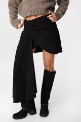 Falda corta de cuero negro con diseño cruzado y detalle de lazo lateral largo que cae sobre una de las piernas.