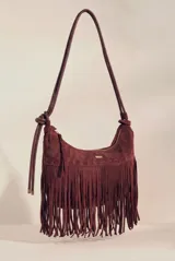 Cartera tipo hobo de gamuza sintética color bordó, con diseño de flecos largos en la parte inferior y correa ajustable con nudo lateral. Cuenta con cierre superior y placa metálica decorativa.