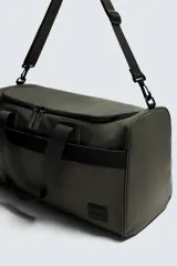 Bolso de viaje tipo duffel bag, color negro, con acabado engomado y costuras visibles. Cuenta con dos asas de mano y una correa de hombro ajustable y extraíble. Posee múltiples compartimentos con cierre de cremallera.