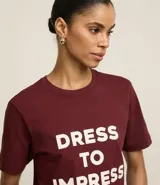Remera color borgoña de algodón, con cuello redondo y mangas cortas. Estampa frontal con la frase "Dress to Impress" en letras mayúsculas blancas.