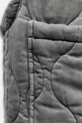 Chaleco gris acolchado con cuello alto, cierre frontal con cremallera metálica, bolsillos de plastrón en delantero y bajo ajustable con cordones.