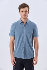 Camisa de piqué lisa color celeste, de manga corta, con cuello camisero y cierre frontal de botones oscuros.
