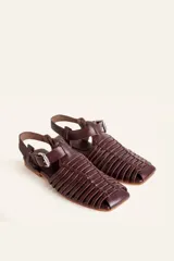 Sandalias planas tipo huarache de cuero negro, con tiras entrelazadas a mano y tira ajustable en el talón con hebilla metálica.
