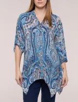 Blusa holgada de poliéster con estampado de arabescos en tonos azules, escote en V con botones frontales, mangas 3/4 y ruedo asimétrico en punta.