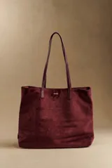 Bolso tipo tote de gran tamaño en color bordó, confeccionado en material con textura similar a la gamuza. Cuenta con doble asa larga para llevar al hombro y una pequeña placa metálica decorativa en el frente.