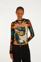 Remera de manga larga y cuello redondo de poliéster y elastano, con un llamativo estampado tropical que incluye un tranvía, vegetación y flores en tonos vibrantes sobre fondo negro.
