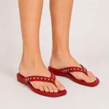 Sandalias de dedo color rojo, con tiras decoradas con tachas metálicas plateadas y suela baja.