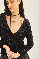 Cardigan negro con escote en V, manga larga y cierre frontal con botones. Presenta un diseño con aplicación de tachas plateadas distribuidas por toda la prenda.