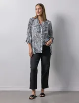 Camisa estampada con hojas en tonos celeste, naranja y verde. Tiene cuello con solapa, abertura central con botones, bolsillos aplicados en la parte delantera y mangas 3/4 con lazo.