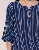 Blusa Erika de algodón con estampado de rayas en tonos azules, rosados y amarillos. Presenta cuello redondo con escote en V y botones frontales, mangas cortas decoradas con una fila de botones en los laterales y dobladillo asimétrico.