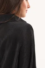 Camisa negra plisada de manga larga con puños vueltos, cuello camisero y cierre frontal de botones claros.