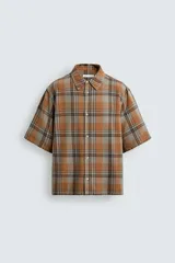 Camisa de corte boxy fit confeccionada en tejido de algodón, con estampado de cuadros en tonos tierra. Presenta cuello solapa, manga corta y cierre frontal de botones.