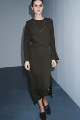 Vestido midi de Zara Woman Collection, color verde oscuro, con cuello redondo, manga larga y detalle de pliegues en el delantero. Presenta un corte recto con abertura frontal en el bajo y cierre lateral con cremallera oculta.