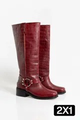 Botas de caña alta en cuero con textura de cocodrilo, color bordó. Presentan un diseño de punta cuadrada, taco bajo y una correa decorativa con argolla metálica y remaches en la zona del tobillo.