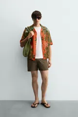 Camisa de corte relajado confeccionada en tejido fluido con mezcla de viscosa y lino. Presenta cuello bowling, manga corta y cierre frontal con botones. Diseño con estampado floral en tonos verdes y naranjas.