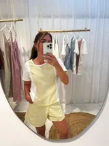 Remera blanca con panel frontal amarillo, detalles de puntilla y corte irregular.