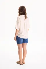 Camisa de lino color beige, de manga corta, con cuello camisero, bolsillos delanteros con solapa y cierre frontal con botones de madera.