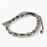 Pulsera ajustable con cordón marrón, compuesta por una alternancia de cuentas esféricas doradas y cuentas facetadas de cristal oscuro.