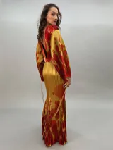 Vestido largo plisado con estampado abstracto en tonos rojo, naranja y dorado, cuello alto y mangas acampanadas. Incluye lazo fino para ajustar en la cintura.