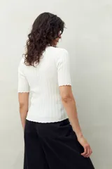 Top negro de manga corta tejido con textura acanalada, cuello alto y terminaciones onduladas.