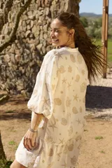 Vestido corto beige con estampado de caracoles y estrellas de mar, cuello camisero con escote en V, mangas tres cuartos y volado en el ruedo.