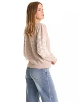 Buzo de punto marca Pinch, color marrón claro, con cuello redondo y mangas largas. Presenta un diseño de flores blancas bordadas a lo largo de las mangas y detalle de frunce en los hombros. Cuenta con puños y ruedo acanalados.