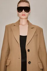 Abrigo largo entallado de Zara Woman Collection, confeccionado en mezcla de lana color tostado. Presenta cuello con solapa de muesca, mangas largas, bolsillos con solapa en el frente, forro interior y cierre frontal de dos botones oscuros.