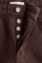Pantalón tipo jean de corte wide leg y tiro medio, confeccionado en denim de algodón rígido color marrón oscuro. Presenta diseño clásico de cinco bolsillos, cierre frontal con botón y cremallera, y piernas amplias con caída recta.