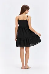 Vestido corto negro de algodón con diseño holgado, escote cuadrado y tirantes finos. Presenta detalles de bordado con perforaciones en toda la prenda y falda con volados en capas.