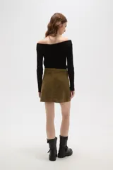Falda mini de corte recto confeccionada en pana de algodón color verde oliva, con cierre frontal de botón metálico y pasacintos.